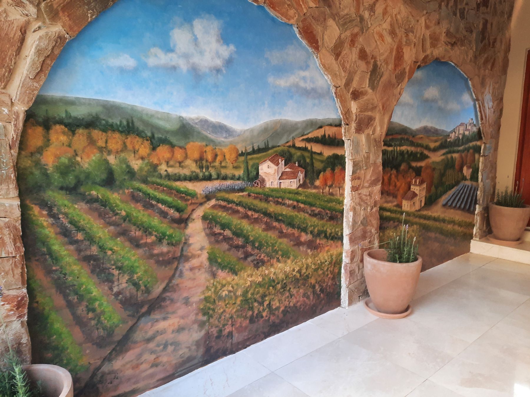 Trompe-l'oeil mural of a Tuscan landscape painted into stone archways on a Bryanston patio