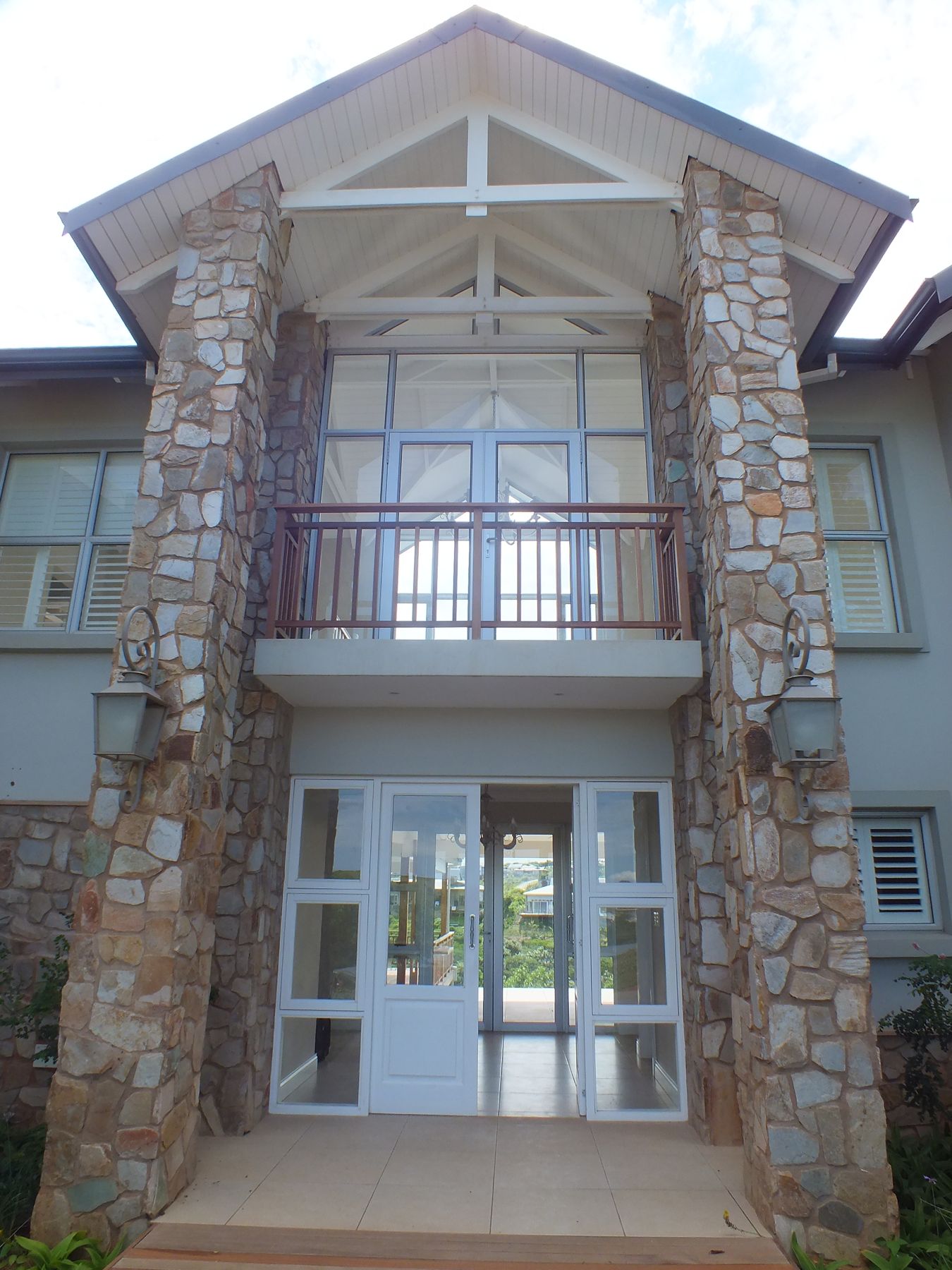 Double-height stone-pillared entrance porch with timber-truss gable at a new house in Simbithi